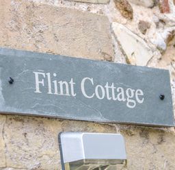 A gray stone sign with Flint Cottage on a stone wall above a light fixture at Flint Cottage in Swaffham