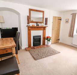 A living room with a wooden fireplace a small rug a wooden table two chairs a television lamp and a window at Flint Cottage in Swaffham