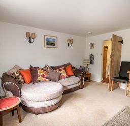 A lounge area with a round sofa and cushions a small table two chairs and wooden door at Flint Cottage in Swaffham