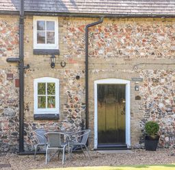 A stone cottage exterior with two windows a black door a small table with four chairs and a potted plant at Flint Cottage in Swaffham
