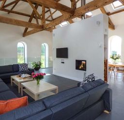 A living room with large dark sofas a coffee table with flowers a TV mounted on a wall and exposed wooden ceiling beams at Capel Dinorwig in Llanberis