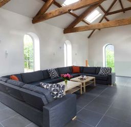A living room with a large dark grey sectional sofa wooden coffee tables and exposed wooden beams at Capel Dinorwig in Llanberis