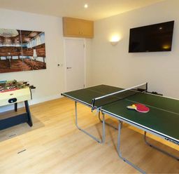 A room with a ping pong table with paddles and ball a foosball table a wall-mounted TV and a triptych wall art at Capel Dinorwig in Llanberis