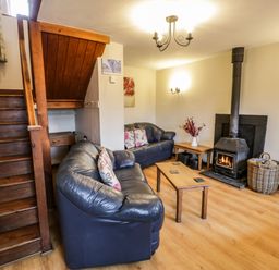 A living room with black leather sofas a wooden coffee table a wood burning stove and wooden stairs at Bwthyn Fedwr Gog in Maerdy near Bala