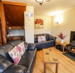 A living room with two leather sofas a wooden coffee table a wood burning stove and a wooden staircase at Bwthyn Fedwr Gog in Maerdy near Bala