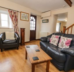 A living room with a black leather sofa and armchair a wooden coffee table and floral curtains at Bwthyn Fed'wr Gog in Maerdy near Bala