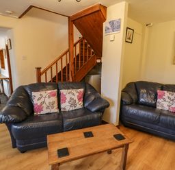 A living room with two black sofas with floral cushions a wooden coffee table and a wooden staircase at Bwthyn Fed'wr Gog in Maerdy near Bala