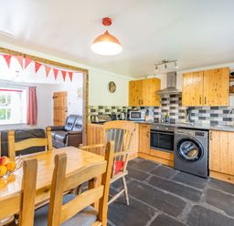 A kitchen with wooden cabinets a dining table with chairs and a living area with leather sofas at No 7 Spark Bridge near Ulverston
