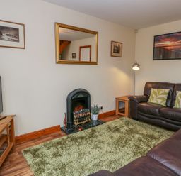 A living room with brown leather sofas green rug a wooden TV stand and a fireplace at Little Venice in Whitby
