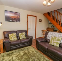 A living room with two brown leather sofas with green patterned cushions and a green rug at Little Venice in Whitby