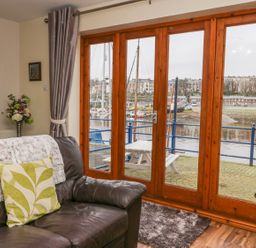 A living room with a leather sofa flowers on a stand and large wooden framed glass doors showing a harbor at Little Venice in Whitby