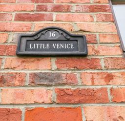 A black house number plaque with number 16 and name Little Venice on a red brick wall next to a window at Little Venice in Whitby
