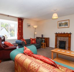 A living room with sofas a coffee table a fireplace and red curtains at Moorside in Horrabridge near Tavistock