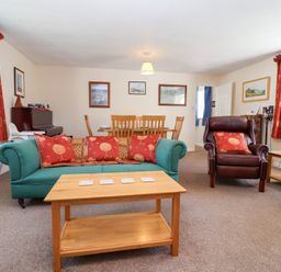A living room with a green sofa and red cushions a brown armchair and a wooden coffee table at Moorside in Horrabridge near Tavistock
