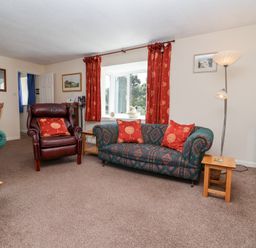 A living room with patterned sofa and armchair with red cushions and a tall lamp at Moorside in Horrabridge near Tavistock