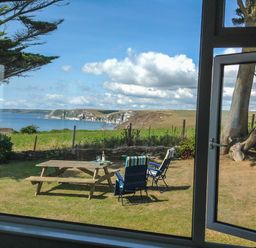 A garden with a wooden picnic table and two lawn chairs overlooking cliffs and the sea at Quarterdeck in Bigbury-on-Sea near Modbury