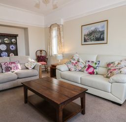 A living room with two sofas with floral cushions a wooden coffee table a wooden chair a display cabinet with plates and a framed picture on the wall at Seascape in Bridlington