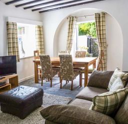 A living room with a sofa and ottoman near a dining table with chairs at The Nook in Bowness-On-Windermere