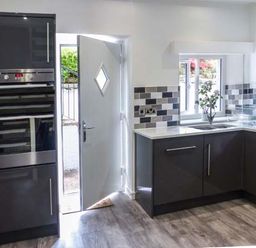 A kitchen with black cabinets a double oven a sink and a partially open door at The Nook in Bowness-On-Windermere