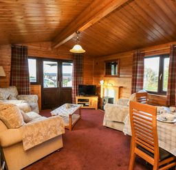 A wooden living room with sofas, a coffee table, a television, a dining table set with dishes and cups at Hawthorne Lodge in Liverton near Danby