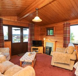 A living room with armchairs a coffee table a television and wooden walls at Hawthorne Lodge in Liverton near Danby