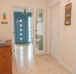 A hallway with a wooden cabinet and blue door with windows at Atlantic Reach in Widemouth Bay
