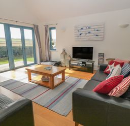 A living room with black leather sofas striped cushions a wooden coffee table television and glass doors at Atlantic Reach in Widemouth Bay