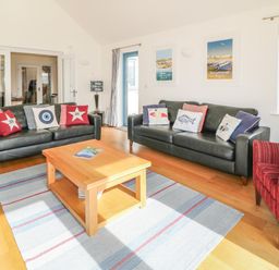 A living room with two black sofas, a red armchair, a wooden coffee table, a rug, and framed beach posters at Atlantic Reach in Widemouth Bay