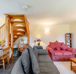 A living room with sofas wooden staircase dining table and bookshelf at Cwmdu Cottage in Cwm-Cou near Newcastle Emlyn