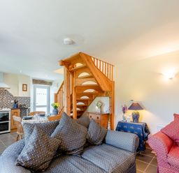A living room and kitchen with blue and red couches wooden dining table and stairs at Cwmdu Cottage in Cwm-Cou near Newcastle Emlyn