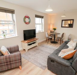 A living room with a grey sofa and a plaid armchair a TV on a white stand and a round dining table with chairs at Sunny Bay in The Bay near Filey