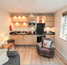 A kitchen with wooden cabinets and black countertop next to a living area with armchair and sofa at Sunny Bay The Bay near Filey