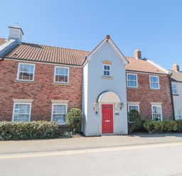 A two story brick house with a red door bushes and windows at Sunny Bay The Bay near Filey