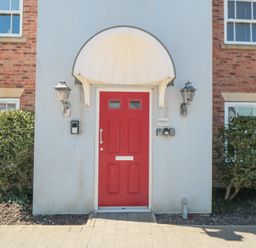 A red front door with an arched white canopy and two wall lanterns flanked by bushes at Sunrise in The Bay near Filey