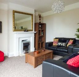 A living room with black leather sofas a wooden coffee table a white fireplace with a gold framed mirror and a wall mounted TV at Westgate Retreat in Hunstanton