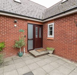 A brick exterior entrance with a dark wooden door two small windows and potted plants at Hurst Green in Ewyas Harold near Hereford
