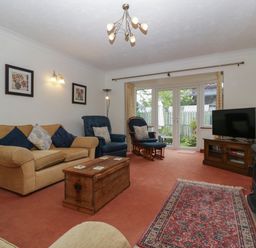 A living room with sofas, a wooden chest table, a rocking chair, a TV on a wooden stand, and glass doors leading outside at Hurst Green in Ewyas Harold near Hereford