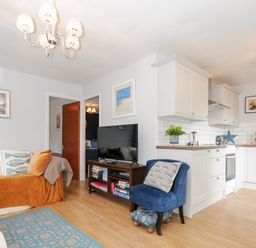 A living room with a sofa a blue chair and a TV next to a kitchen with white cabinets at No 1 The Heathers Rosecraddoc Lodge near Liskeard