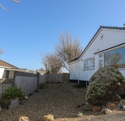 An exterior view of a single-story house with gravel yard and shrubbery at Tegfan in Trearddur Bay