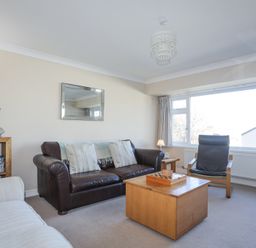 A living room with a brown leather sofa two cushions a wooden coffee table a black armchair and a bookshelf at Tegfan in Trearddur Bay