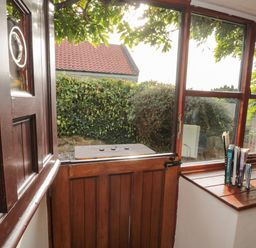 A wooden stable door open to a garden with hedge and bushes seen through window at Goathland Cottage Ruswarp near Whitby