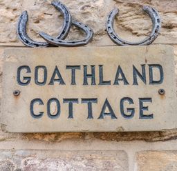 A stone plaque with Goathland Cottage text and three horseshoes above on a stone wall at Goathland Cottage Ruswarp near Whitby