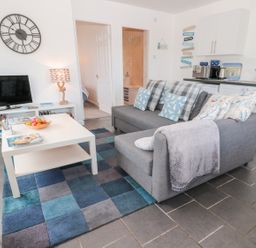 A living room with a gray sofa and pillows beside a white coffee table and a television at Bracken Barn Cottage Widdrington near Amble