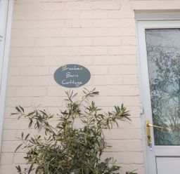 An exterior wall with a sign reading Bracken Barn Cottage next to a door with frosted glass and a plant in front of the wall at Bracken Barn Cottage Widdrington near Amble
