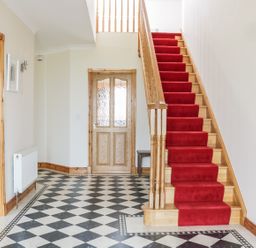 An entryway with black and white checkered floor a wooden staircase with a red runner and wooden door at McGuire's Cottage Barnatra County Mayo