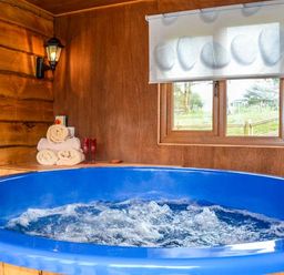 An indoor hot tub with bubbling water near a window and wooden walls with towels and glasses on a shelf at Brynhir Farm in Howey near Llandrindod Wells
