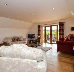 A living room with sofas armchairs a television and glass doors leading to a patio at Brynhir Farm in Howey near Llandrindod Wells
