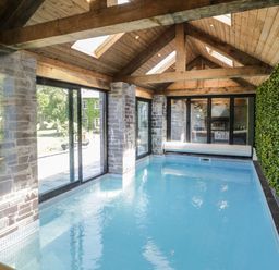 An indoor swimming pool with glass doors stone walls and a green wall at Bryn Derwen Bethesda near Caernarfon