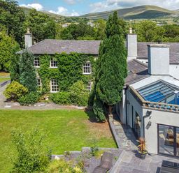 A house with ivy on one side and a glass roof extension surrounded by trees and grass at Bryn Derwen in Bethesda near Caernarfon
