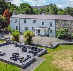 A large two-story house with a stone patio and outdoor seating area surrounded by trees at Bryn Derwen Bethesda near Caernarfon